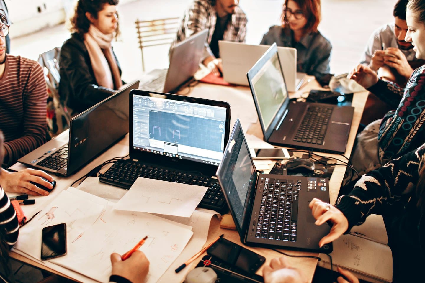 Vielfältige junge Erwachsene arbeiten gemeinsam an Laptops an einem Holztisch.