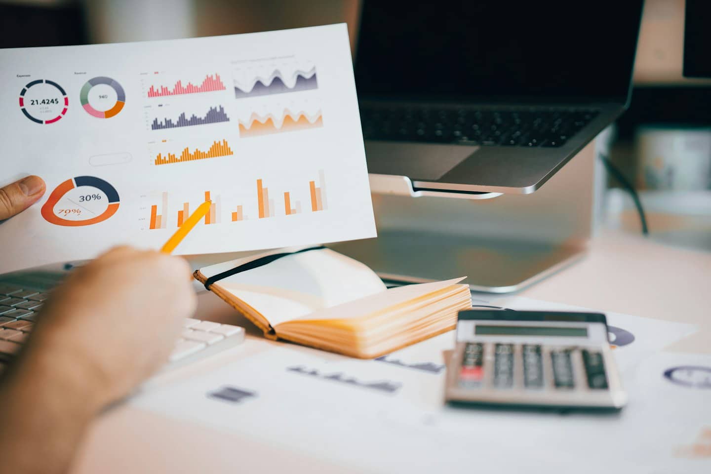 Eine Person analysiert mit einem gelben Bleistift auf einem Schreibtisch Geschäftsdaten-Diagramme.